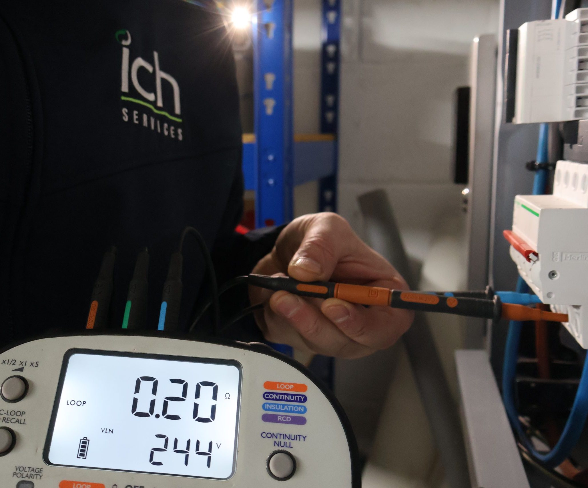 An ICH staff member holding a multimeter and its probes, performing electrical testing on a component.